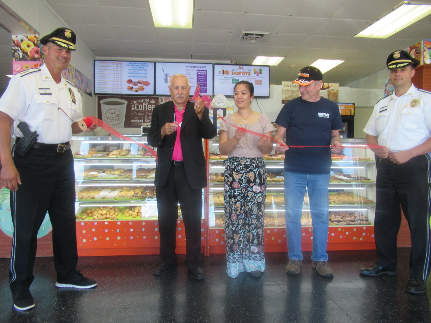 OFFICIAL OPENING: With JPD Chief Joseph P. Razza (left) and Deputy Chief Mark Vieira (right) holding a red ribbon alongside Sophal Cheng and Bob Moulton, Mayor Joseph Polisena performs the ceremonial cutting at last Thursday’s Grand Opening of Rhode Island Homemade Donuts in Johnston.